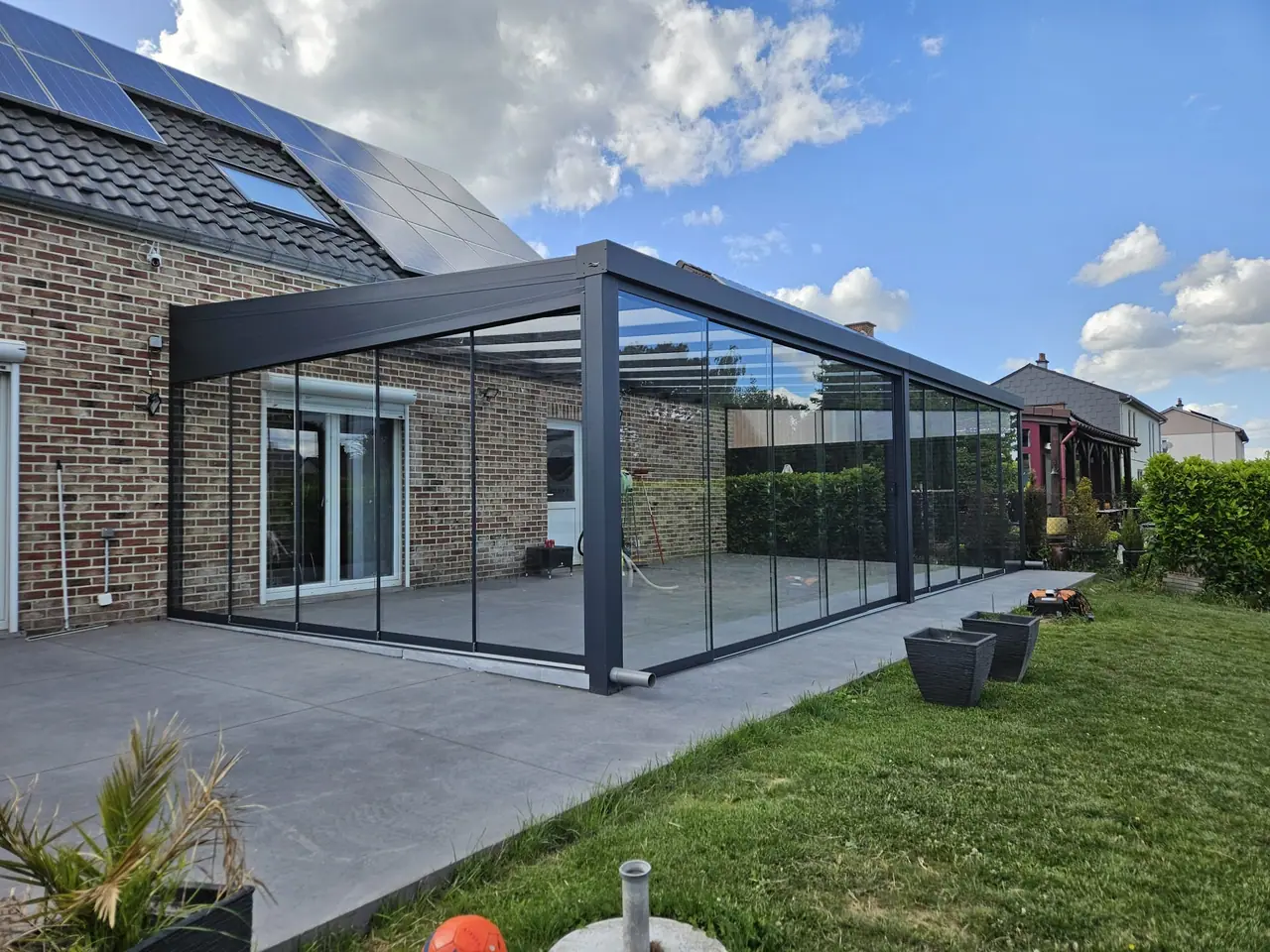 Anthrazitfarbene Aluminium-Terrassenüberdachung mit Glasdach und Glasschiebewänden ringsum
