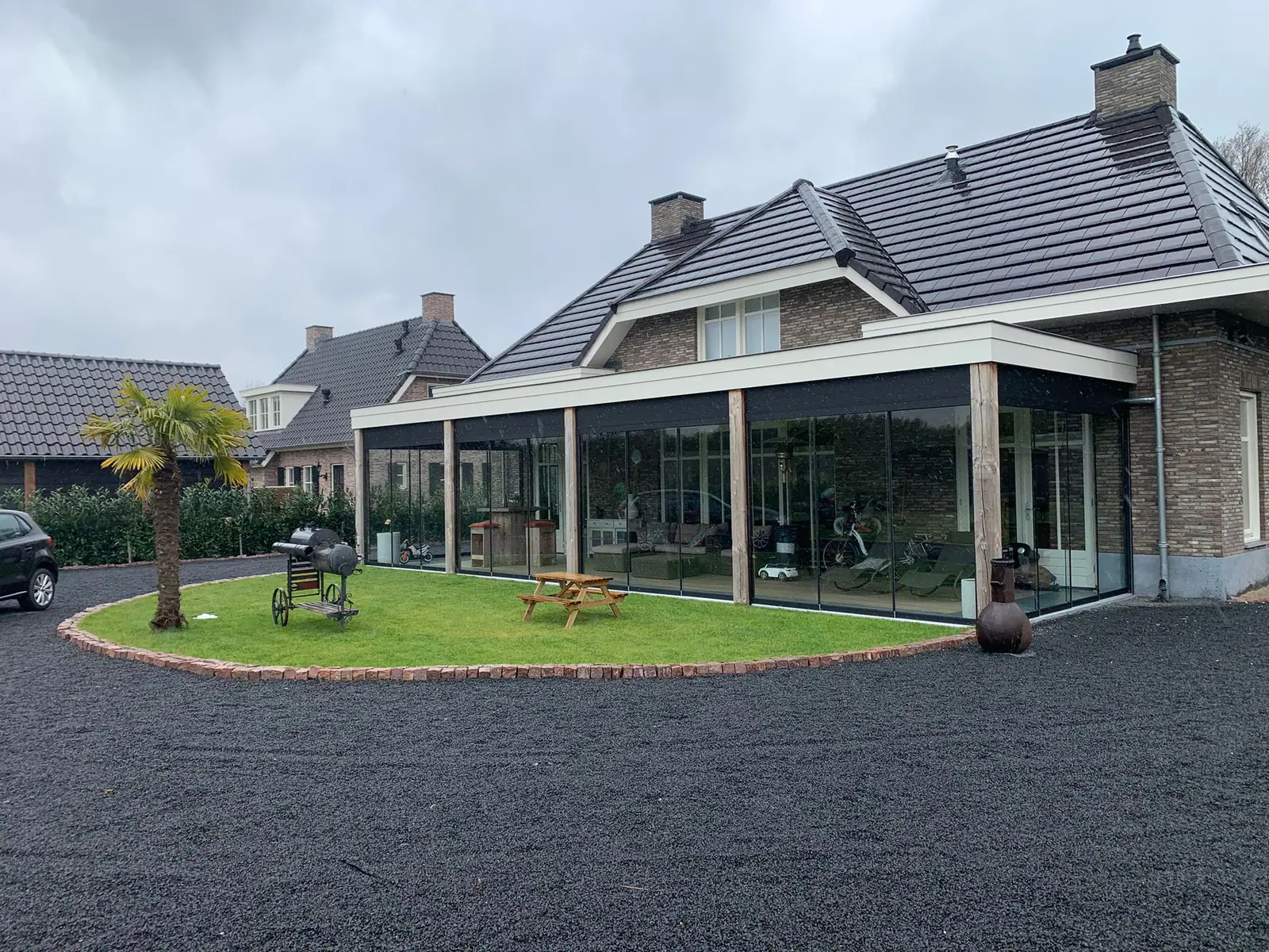 Breite Terrassenüberdachung entlang der Fassade mit Holzstützen und Glasschiebewänden, um die Ecke laufend