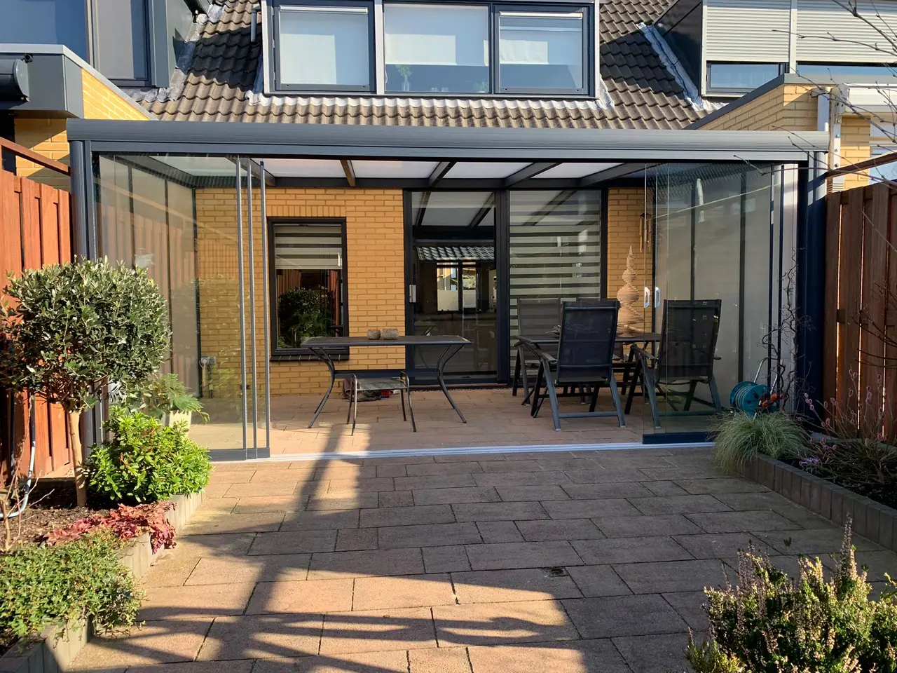 Aluminium-Terrassenüberdachung mit Glasschiebewänden an einer sonnigen Terrasse
